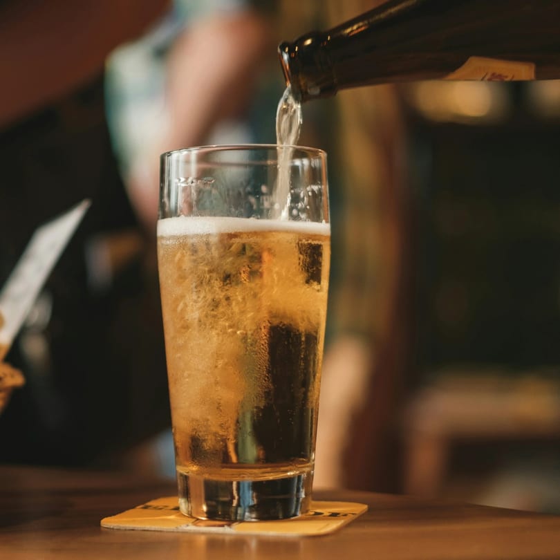 Beer pouring from a bottle into a frosty glass on a wooden bar top.