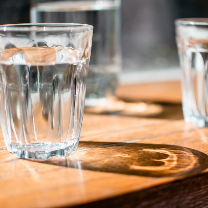 Three glasses of water on a wooden table, with sunlight creating interesting shadows.