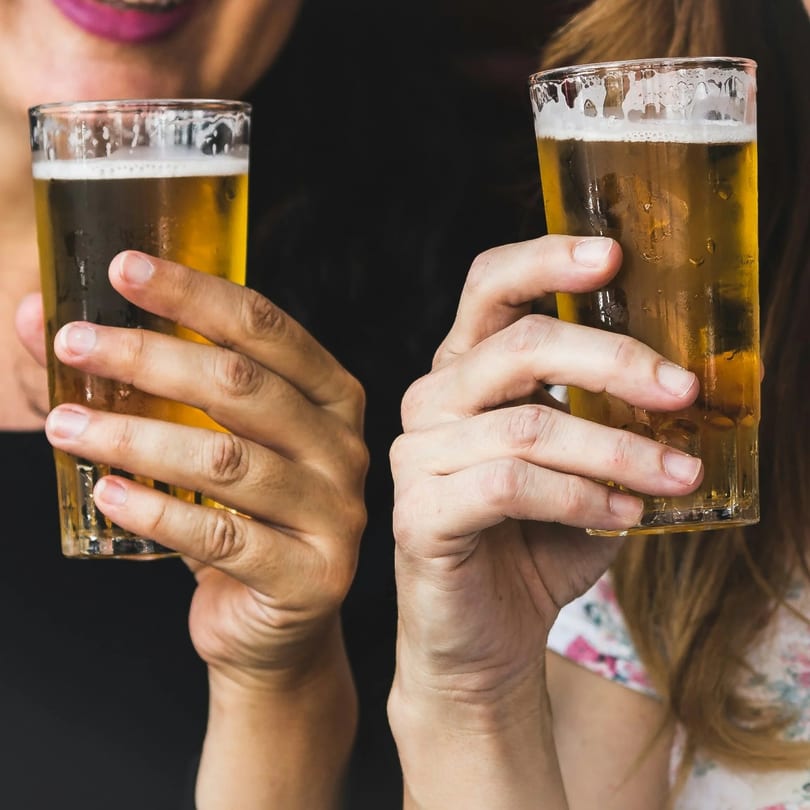 Two people holding up glasses of golden beer with foamy tops, ready for a toast.